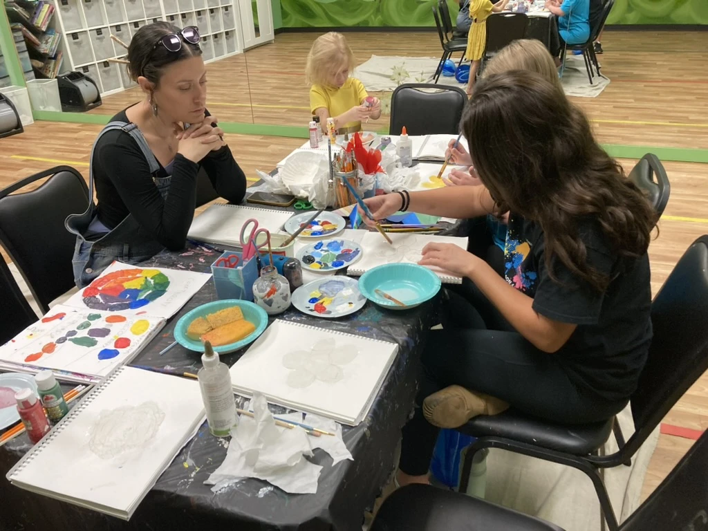 ArtHaus students painting color wheels and flowers around the art table