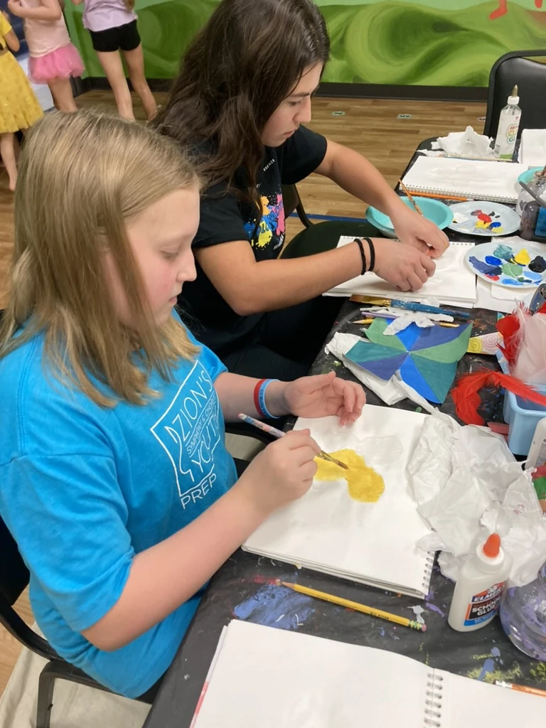 Two ArtHaus students painting in their sketchbooks