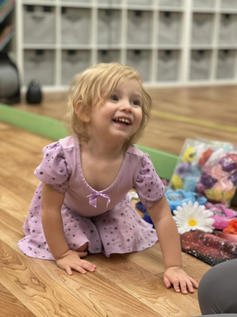A giggling toddler in a purple polka dot leotard during class