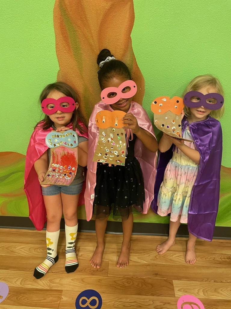 Summer campers in capes and masks showing off their crafts