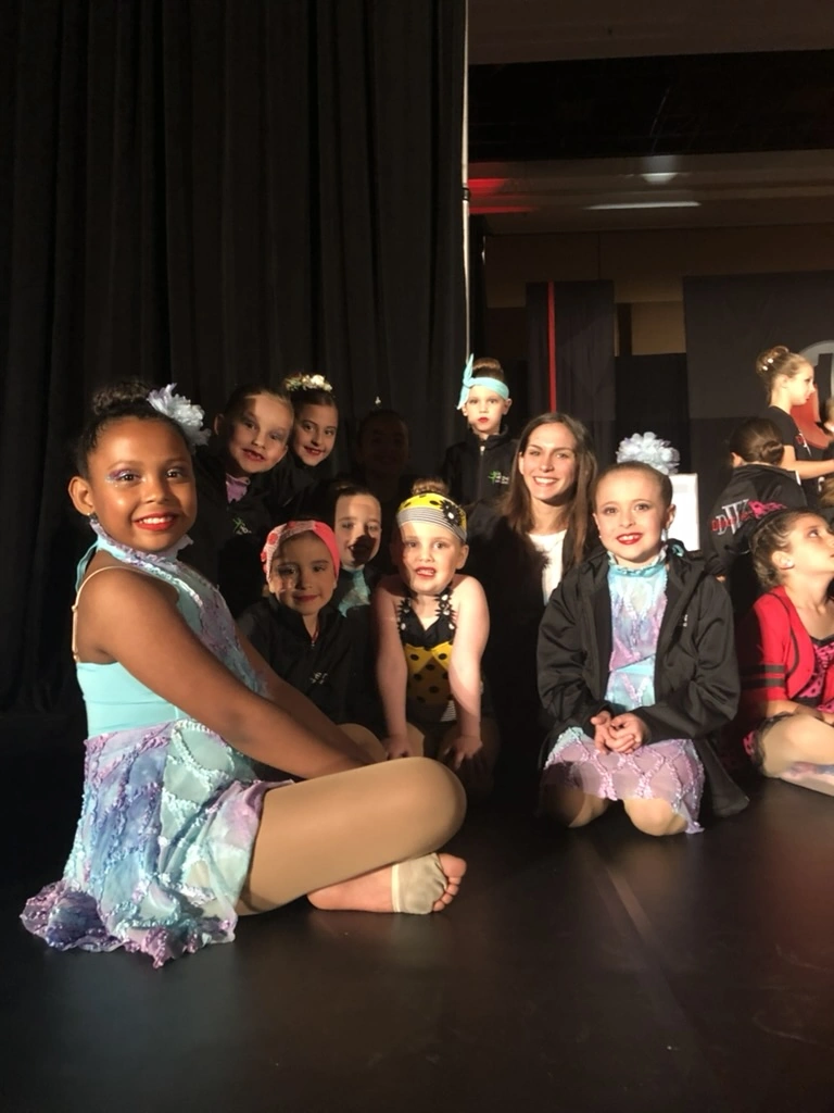 Company dancers and their teacher smiling backstage at a competition