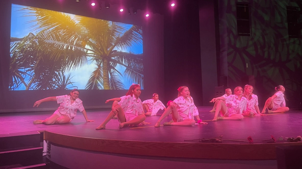 Company dancers in pink pajamas performing a floor sequence with a palm tree backdrop