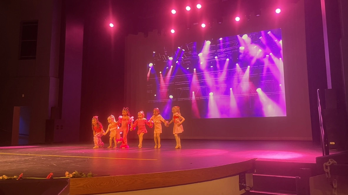 Mini company dancers in pink taking their bow under stage lights