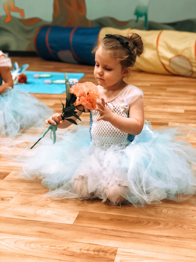A tiny ballerina in a blue tutu admiring her flower prop
