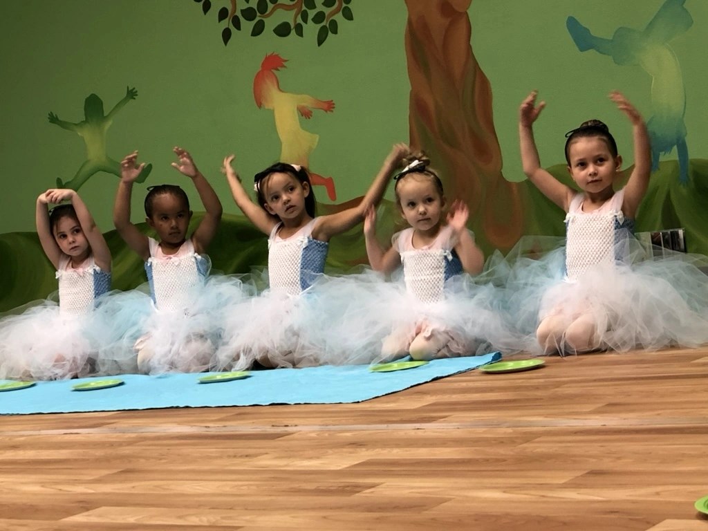 A row of little ballerinas in white tutus with arms up in Once Upon a Ballet