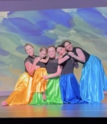 Dancers in bright satin skirts hugging after their number at Ovation Theatre