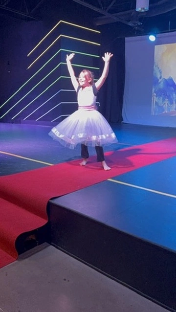 A young dancer in a white tutu takes a bow on the red carpet at Ovation Theatre