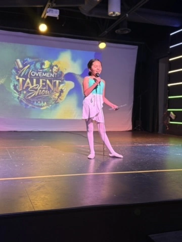 A young singer performing at The Movement Talent Show in Ovation Theatre